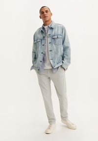 Chaqueta de mezclilla azul clara con dos bolsillos en el pecho, camisa de botones gris debajo, pantalones grises y zapatillas blancas. Diseño simple, corte relajado.