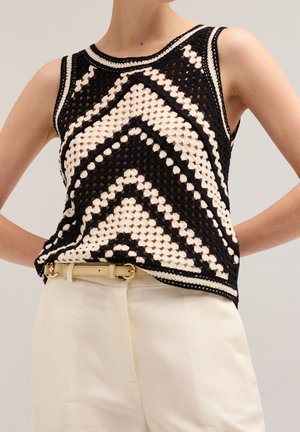 Haut crochet sans manches noir et crème avec motif géométrique, porté avec un pantalon taille haute crème et une ceinture beige.