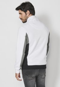 Sweatshirt color-block bianco e grigio con colletto alto, caratterizzato da una texture morbida e una vestibilità attillata. Accenti neri sui lati e sull'orlo.