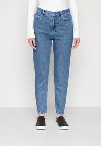 Ljust blå denimjeans med hög midja, rak benform, fem fickor och minimal blekning, kombinerat med svarta slip-on skor.