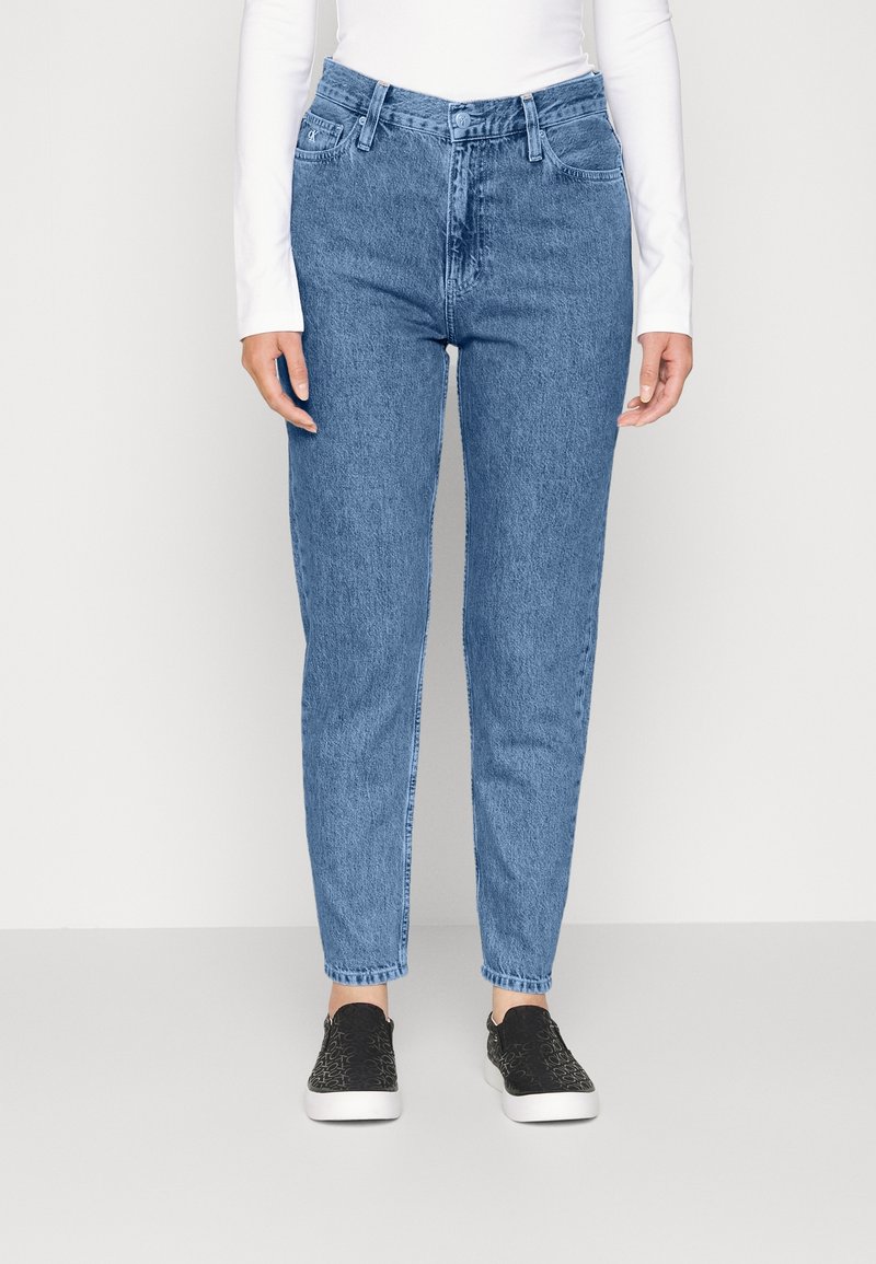 Ljust blå denimjeans med hög midja, rak benform, fem fickor och minimal blekning, kombinerat med svarta slip-on skor.