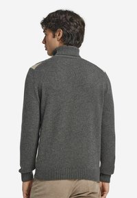 Grau gestrickter Pullover mit hohem Kragen, gerippten Ärmeln und Saum. Verfügt über helle beige Akzente an den Schultern. Strickstruktur und taillierte Passform.