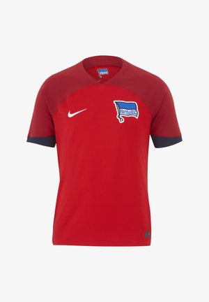 Maglia sportiva rossa Nike con scollo a V, caratterizzata da accenti blu sulle maniche e dal logo del Hertha BSC sul petto. Tessuto liscio.