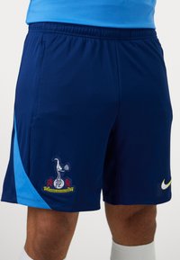 Marine atletiske shorts med lyseblå accent på siden. Har et logo patch og Nikes karakteristiske swoosh-logo i gul. Letvægtsmateriale.