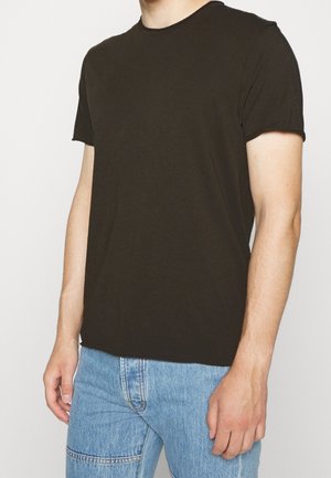 Mężczyzna ubrany w gładki czarny T-shirt z krótkim rękawem i jasnoniebieskie dżinsy, stoi na tle jednolitego białego tła.