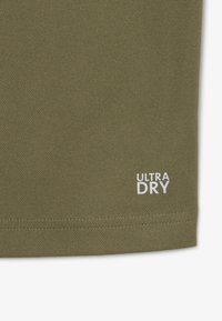 Oliivinvihreä kangas, jossa on teksturoitu pinta, ja oikeassa alakulmassa valkoinen "ULTRA DRY" -label.