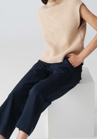 Beige ribbad stickad ärmlös tröja med hög krage, i kombination med marinblå skräddarsydda byxor, som har en avslappnad passform och raka ben.