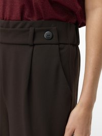 Rjave hlače po meri z bočnimi žepek. Imajo raven sprednji del in vidni črni gumb na pasu. Gladek tekstura, prilagojen kroj.