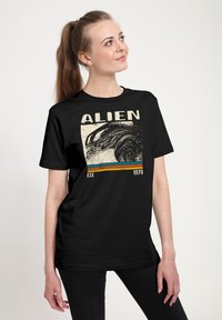 Czarna koszulka z ilustracją obcego stworzenia, z napisem "ALIEN" w pogrubionym tekście oraz "EST. 1979" poniżej w kontrastowych kolorach.
