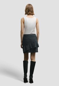 Biely tielkový top v kombinácii s vrstvenou tmavou sukňou s volánmi a diagonálnym strihom, doplnený vysokými čiernymi čižmami na vysokom opätku.