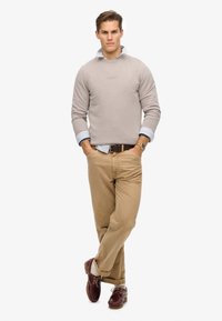 Beige sweatshirt med rund hals, lyseblå ternet skjorte under, khaki bukser og bordeauxfarvede sko med træsål og snørebånd.