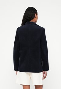 Granatowa marynarka z sztruksu o dopasowanym kroju, z długimi rękawami, klapami z wycięciem oraz rozcięciem z tyłu. Brak widocznych ozdobników i wzorów; gładka faktura.