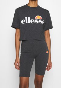 Mörkgrå kortärmad t-shirt med vitt "ellesse"-logotyp och orange solgrafik, tillsammans med matchande mörkgrå cykelshorts med logodetalj.