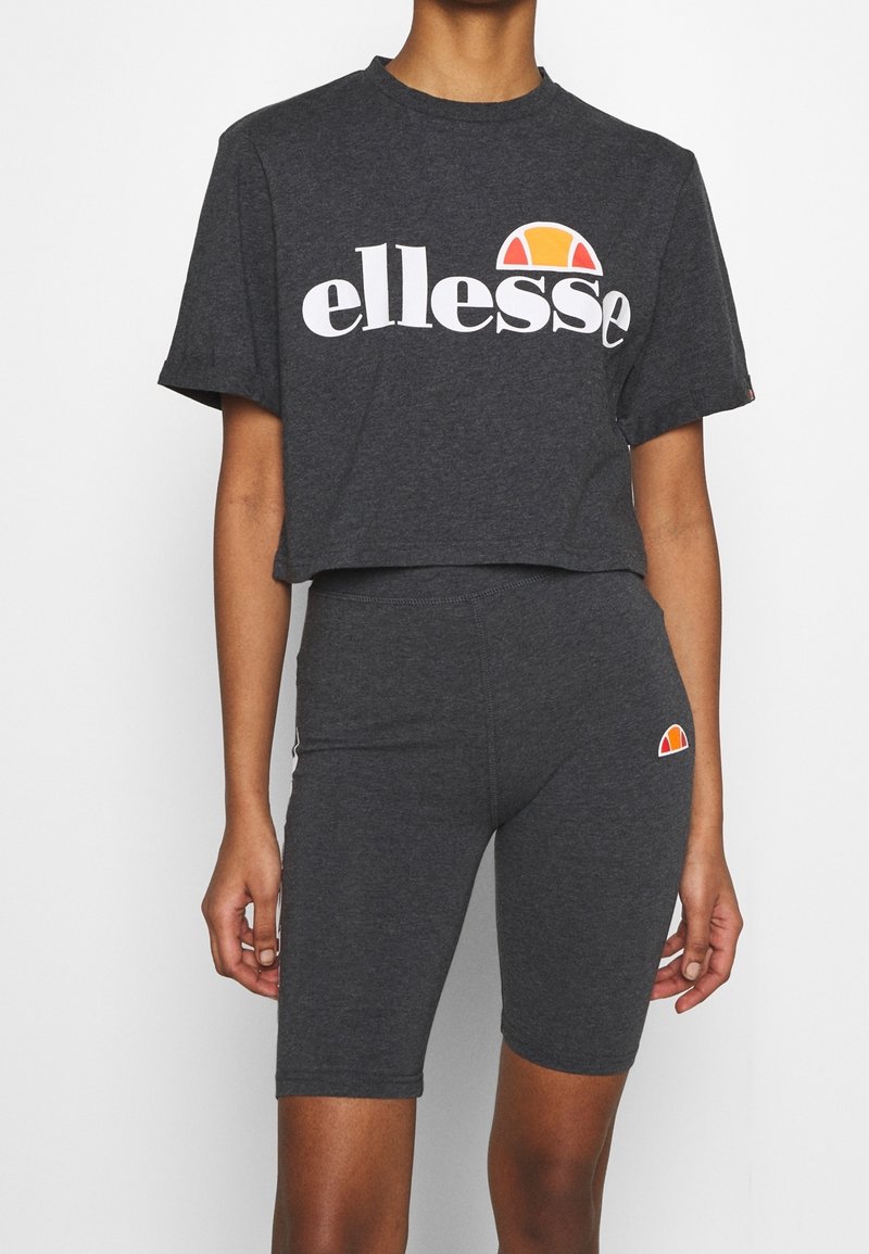 Mörkgrå kortärmad t-shirt med vitt "ellesse"-logotyp och orange solgrafik, tillsammans med matchande mörkgrå cykelshorts med logodetalj.