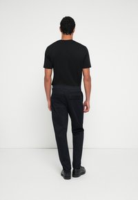 Fekete pamut póló sötét nadrággal párosítva. A nadrágnak két hátsó zsebe van, szabott fazonú, melyet fekete cipő egészít ki.