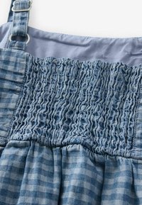 Sininen ruudullinen mekko, jossa on rypytetty yläosa ja säädettävät hihnat, pehmeä rakenne ja virtaava helma. Pystysuuntaisia ja vaakasuuntaisia kuvioita.