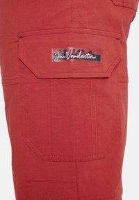 Rote Baumwoll-Shorts mit Cargo-Style, die eine große Seitentasche mit einem Überlagerungsetikett, gestickten Akzenten und einer strukturierten Form aufweisen.