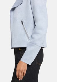 Jasnoniebieska kurtka z ekoskóry z kołnierzem z klapami, boczną kieszenią na zamek i krótkim fasonem. Gładka faktura, dopasowane rękawy oraz surowe wykończenie na dole.