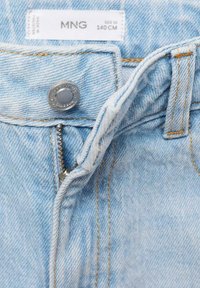 I jeans in denim azzurro chiaro presentano un bottone e una chiusura lampo argentati, con cuciture arancioni a contrasto lungo le cuciture. Etichetta della taglia visibile.