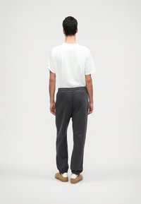 Pelēki sporta bikses ar elastīgu jostasvietu, piedurkņu un sānu kabatām, apvienotas ar vienkāršu baltu T-kreklu un ikdienas apaviem.