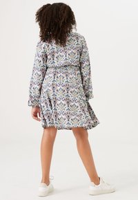 Langärmliges Kleid mit elastischem Bund, das ein buntes Blumen- und geometrisches Muster auf hellem Hintergrund zeigt, kombiniert mit weißen Sneakers.