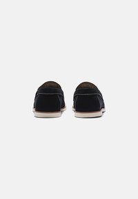 Zapatos tipo slip-on de ante azul marino con costuras blancas en contraste, punta redonda y suela de goma ligera. Textura suave y diseño minimalista.
