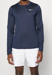 Merinavy siniset pitkähihaiset urheilupaidat, joissa on neljännesvetoketju ja pyöreä kaula-aukko, valmistettu kevyestä kankaasta. Rinnassa pieni valkoinen Nike-logo.