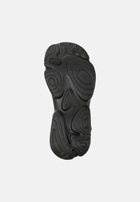 Black rubber shoe sole with a textured pattern featuring wavy and oval shapes, providing grip and flexibility. Contains branding detail.