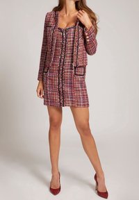 Roze en multikleuren tweed jasje jurk met knopen aan de voorkant, zwarte randen en zakken. Korte mouwen en een aangesloten silhouet. Rode hakken.