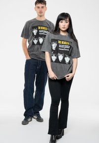 Gray cotton t-shirts feature The Beatles graphic with a yellow text and black accents. Slim black pants worn by the models.