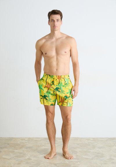 Un short de bain jaune avec un motif de palmier, doté d'une taille élastique et d'un cordon de serrage. Le matériau semble léger et à séchage rapide.
