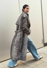 Kapsáč s leopardím vzorem, s páskem v pase, širokými klopami a dlouhými rukávy, spárovaný s světle modrými zvonovými džíny a plochými botami.