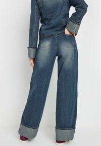 Wijde denim jeans in donkerblauw met vervaagde accenten, omgeslagen broekspijpen en een vijf-pocket ontwerp. Geweven stof met traditionele stikseldetails.