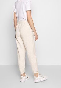 Licht beige sweats met een relaxte pasvorm, elastische tailleband en gebreide enkels. Gepaard met witte sneakers en een eenvoudig wit T-shirt.