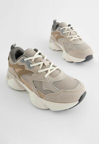 Beige mesh sneakers med suede-detaljer, teksturerede overlays, rund tå og en tykk hvid sål med en sort gummihæl.