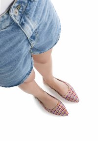 Bailarinas tricolores tejidas con una puntera afilada y un diseño de parte trasera abierta, con matices en rosa, púrpura y amarillo. Combinadas con pantalones cortos de mezclilla.