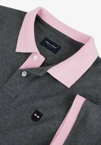 Polo gris foncé avec col rose clair, bordure des manches, boutons blancs et petit logo brodé noir et rose sur la poitrine.