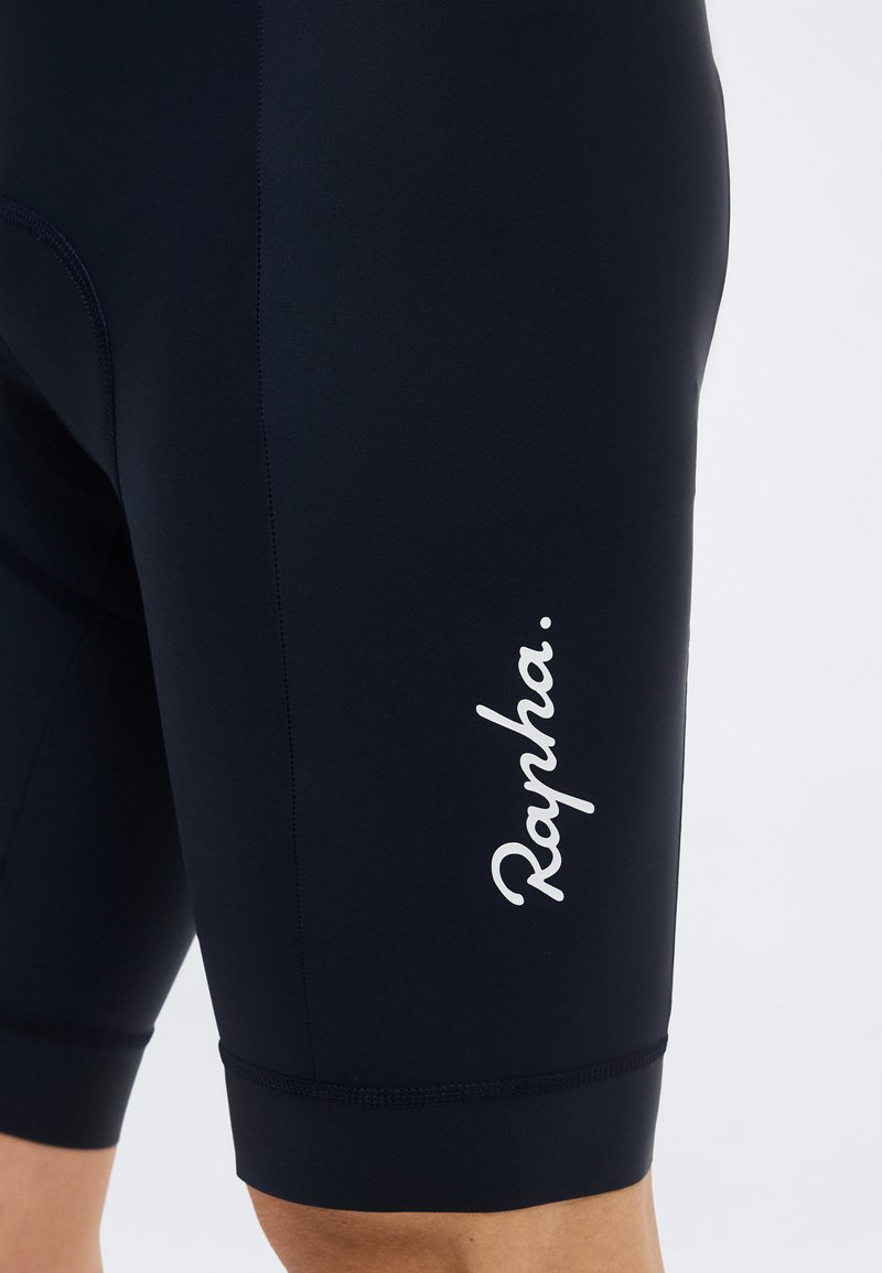 Close-up of a person's thigh wearing black cycling shorts with white "Rapha" branding on the side.
