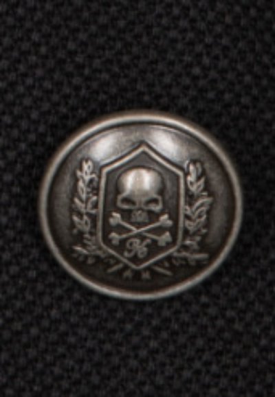 Metallknopf mit einer matten silbernen Oberfläche, der einen Schädel, gekreuzte Knochen und Lorbeerakzente innerhalb einer schildförmigen Umrandung zeigt, auf einem strukturierten schwarzen Hintergrund.