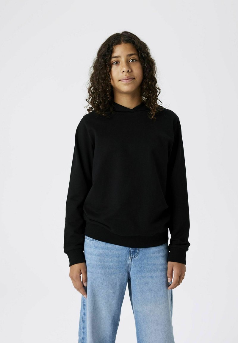 Felpa nera con cappuccio, dal fit rilassato, con polsini e orlo a costine. Abbinata a jeans a gamba larga di colore blu chiaro. Design minimalista su uno sfondo neutro.