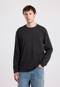Black long-sleeve shirt with a round neckline. Made of soft fabric, featuring a relaxed fit and smooth texture. Worn with blue jeans.