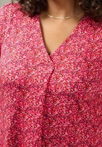 Pink floral-patterned top made of soft fabric, featuring a V-neck and a button detail at the bust. Lightweight and textured design.