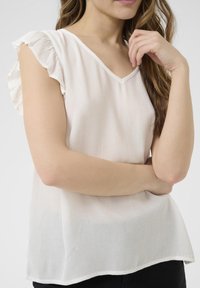 Blouse légère, rose pâle, avec un col en V, un tissu texturé et des manches volantées. Présente une coupe ample et un ourlet droit.