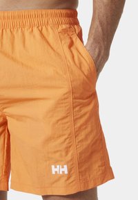 Oranžové plavkov é šortky vyrobené z lehkého materiálu. Elastický pas, postranní kapsy a bílý akcent s logem na dolní levé straně.