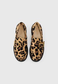 Lepoardmønster slip-on sko med en gullspenne, laget av en tan og svart semsket skinnmateriale, og en teksturert svart såle.