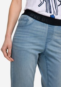 Jeans de denim azul claro con una cinturilla elástica negra que presenta el texto "amor". Los jeans tienen una pierna ajustada y bolsillos laterales.