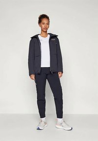 Σκοτεινό αδιάβροχο μπουφάν με κουκούλα, δύο μπροστινές τσέπες, σε συνδυασμό με ναυτικά παντελόνια και αθλητικά παπούτσια. Απλός σχεδιασμός, λειτουργικά χαρακτηριστικά.