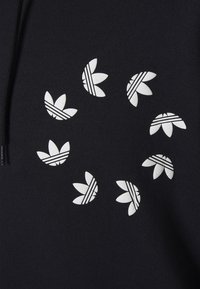 Juodas džemperis su pasikartojančiu baltu trefoil formų grafiniu raštu. Kiekviena trefoil forma turi linijų raštus. Minkšta tekstūra, kasdieniškas dizainas.