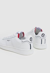 Sneakers bianchi con tomaia in pelle liscia, dettagli perforati, accenti blu navy e logo sul tallone. Fodera interna rossa.