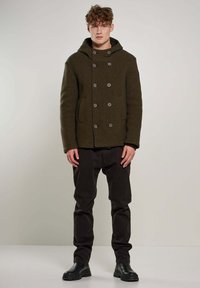 Olijfgroen peacoat met een capuchon, dubbelgeknoopte knopen en zijzakken, gecombineerd met donkere broeken en zwarte gevechtslaarzen.